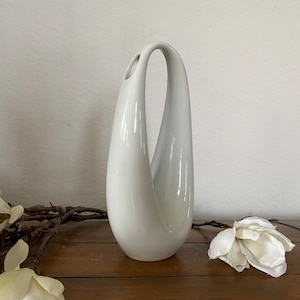 May include: A white ceramic vase with a unique, modern design. The vase has a smooth, glossy finish and a curved, organic shape.