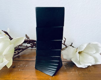 Può includere: Una bottiglia nera rettangolare impilabile con un design geometrico. La bottiglia è realizzata in un materiale liscio e lucido.