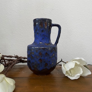 Könnte beinhalten: Eine blaue und braune Keramikvase mit texturierter Glasur. Die Vase hat einen runden Körper und einen einzelnen Henkel.