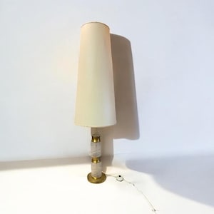 Könnte beinhalten: Eine Vintage-Stehlampe mit cremefarbenem, konischem Schirm. Die Lampe hat einen dekorativen Sockel mit goldenen Akzenten und eine strukturierte, hellfarbige Säule. Die Lampe ist etwa 152 cm hoch.