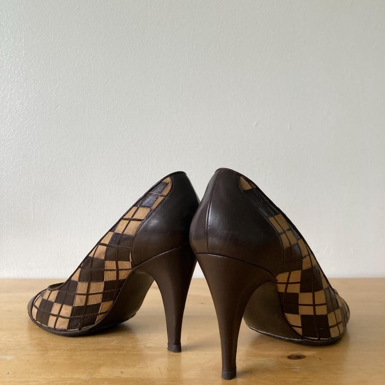 Puede incluir: Un par de zapatos de tac&oacute;n marr&oacute;n. Los zapatos tienen un patr&oacute;n geom&eacute;trico en la parte delantera y los lados, con un tac&oacute;n y ribete marr&oacute;n oscuro. Los zapatos son de cuero y tienen la punta afilada.