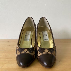 Puede incluir: Un par de zapatos de tac&oacute;n alto marrones y beige con un patr&oacute;n de diamantes en los laterales. La puntera y el tal&oacute;n son de color marr&oacute;n liso. El interior es dorado y la etiqueta dice "Valentino Garavani".