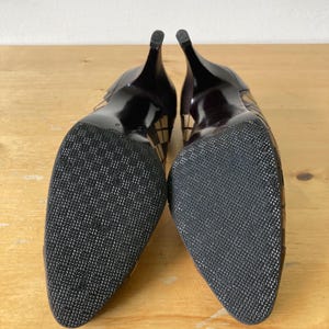 Puede incluir: Par de zapatos de tac&oacute;n negros con suelas texturizadas. Los tacones son delgados y oscuros, con un patr&oacute;n de cuadros en los laterales. Los zapatos tienen un dise&ntilde;o de punta puntiaguda y las suelas son negras con un patr&oacute;n texturizado.