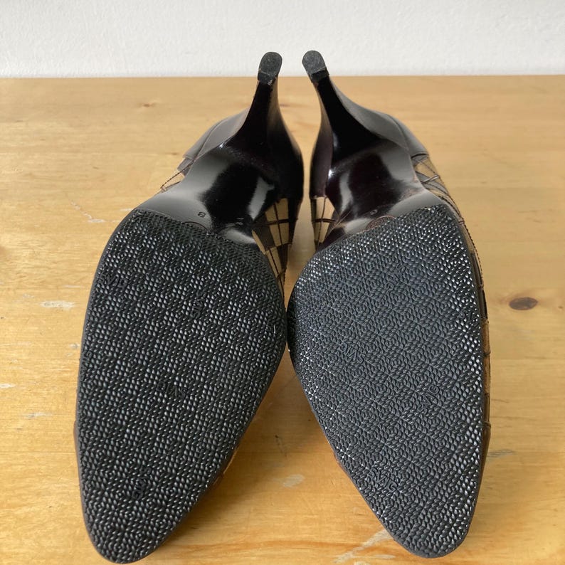 Puede incluir: Par de zapatos de tac&oacute;n negros con suelas texturizadas. Los tacones son delgados y oscuros, con un patr&oacute;n de cuadros en los laterales. Los zapatos tienen un dise&ntilde;o de punta puntiaguda y las suelas son negras con un patr&oacute;n texturizado.