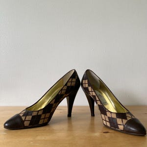 Puede incluir: Un par de zapatos de tac&oacute;n alto con un patr&oacute;n de diamantes marr&oacute;n y beige. Los zapatos tienen una punta puntiaguda y un tac&oacute;n de aguja. El interior del zapato es dorado.