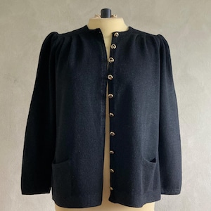 May include: A dark gray cardigan with a round neckline and long sleeves. The sweater features gold-colored buttons down the front and two front pockets. The garment is displayed on a mannequin.