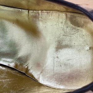 Puede incluir: Primer plano del interior de un zapato, con una plantilla dorada. La plantilla muestra signos de desgaste, con arrugas y decoloraci&oacute;n visibles. El borde del zapato es negro.