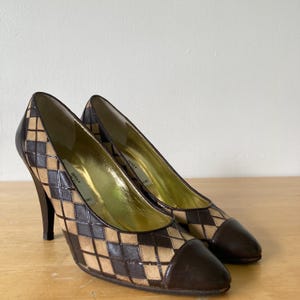 Puede incluir: Un par de zapatos de tac&oacute;n alto con un estampado de rombos marr&oacute;n y beige. La puntera y el tal&oacute;n son de color marr&oacute;n oscuro liso. El interior es dorado. Los tacones miden unos 10 cm.