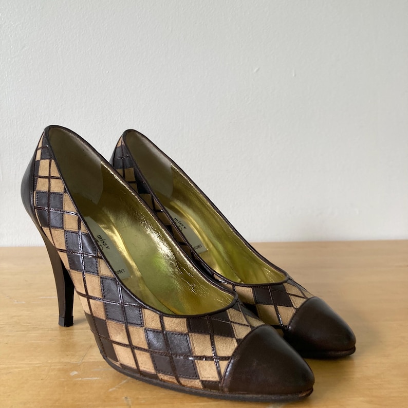 Puede incluir: Un par de zapatos de tac&oacute;n alto con un estampado de rombos marr&oacute;n y beige. La puntera y el tal&oacute;n son de color marr&oacute;n oscuro liso. El interior es dorado. Los tacones miden unos 10 cm.