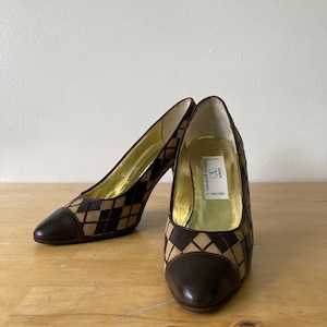 Puede incluir: Un par de zapatos de tac&oacute;n alto marrones y beige con un patr&oacute;n de diamantes. La puntera y el tal&oacute;n son de color marr&oacute;n liso. El interior es dorado y la etiqueta dice "Valentino Garavani".