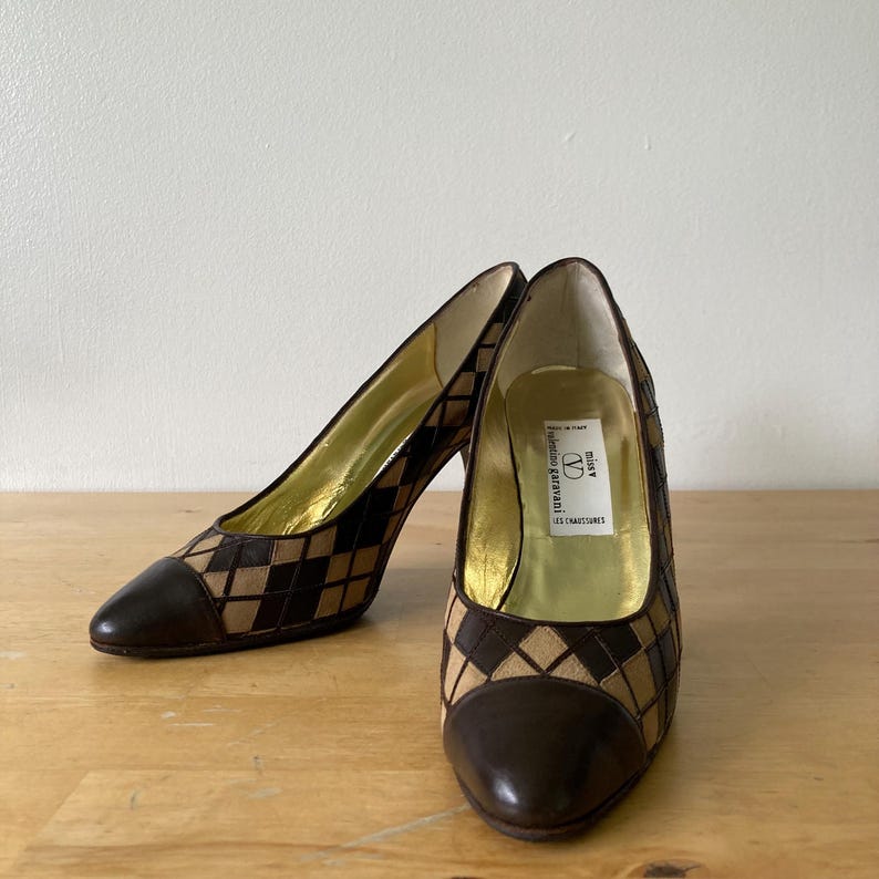 Puede incluir: Un par de zapatos de tac&oacute;n alto marrones y beige con un patr&oacute;n de diamantes. La puntera y el tal&oacute;n son de color marr&oacute;n liso. El interior es dorado y la etiqueta dice "Valentino Garavani".