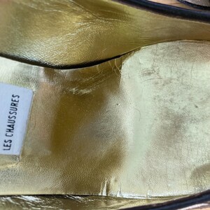 Puede incluir: Primer plano del interior de un zapato con una plantilla dorada. El interior del zapato tiene un aspecto desgastado. Se ve una etiqueta blanca con el texto "LES CHAUSSURES".