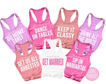 May include: A collection of seven racerback tank tops in various colors, including pink, white, and peach. Each tank top has a different phrase printed on the front in white or pink, such as "Dance on Tables" and "Get Married."