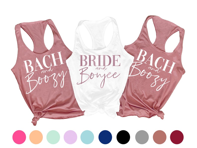 May include: Three tank tops with white text on a pink background. The text on the white tank top reads "Bride and Bonjee" in pink lettering. The text on the two pink tank tops reads "Bach and Boozy".