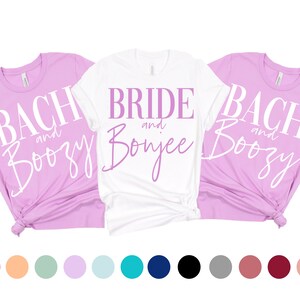 May include: Three t-shirts with different text designs. The white t-shirt says "Bride and Bonjee" in purple text. The two lavender t-shirts say "Bach and Boozy" in white text.
