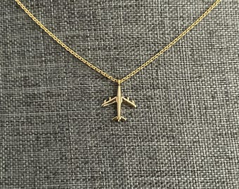Op de afbeelding: Een gouden ketting met een klein vliegtuighanger.