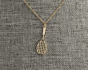 May include: A gold tennis racket pendant necklace with clear crystal accents.