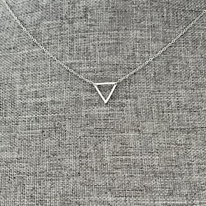 May include: A silver-toned necklace featuring a delicate chain and a single, open-frame triangle pendant. The pendant is centered on the chain, which consists of small, interconnected oval links. The metal has a polished, reflective finish throughout.