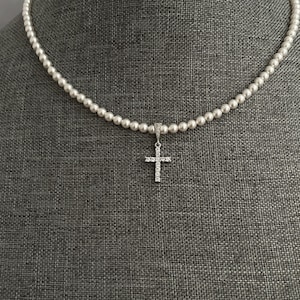May include: A white pearl necklace with a small silver cross pendant encrusted with clear cubic zirconia stones.