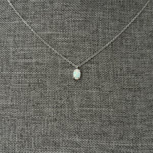 May include: A delicate silver-toned chain necklace featuring a single, small, oval-shaped opal pendant. The iridescent stone is held in a simple four-prong setting, suspended from a thin, polished metal link chain that extends across the frame.
