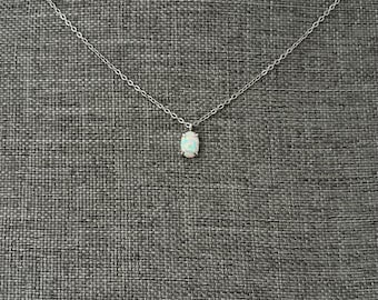 Puede incluir: Un delicado collar de cadena en tono plateado con un único colgante de ópalo pequeño y ovalado. La piedra iridiscente se sujeta con un engaste sencillo de cuatro garras, suspendida de una fina cadena de eslabones metálicos pulidos.