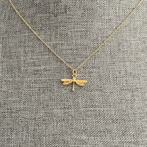 May include: A gold chain necklace with a dragonfly pendant. The dragonfly is detailed and has a delicate design.