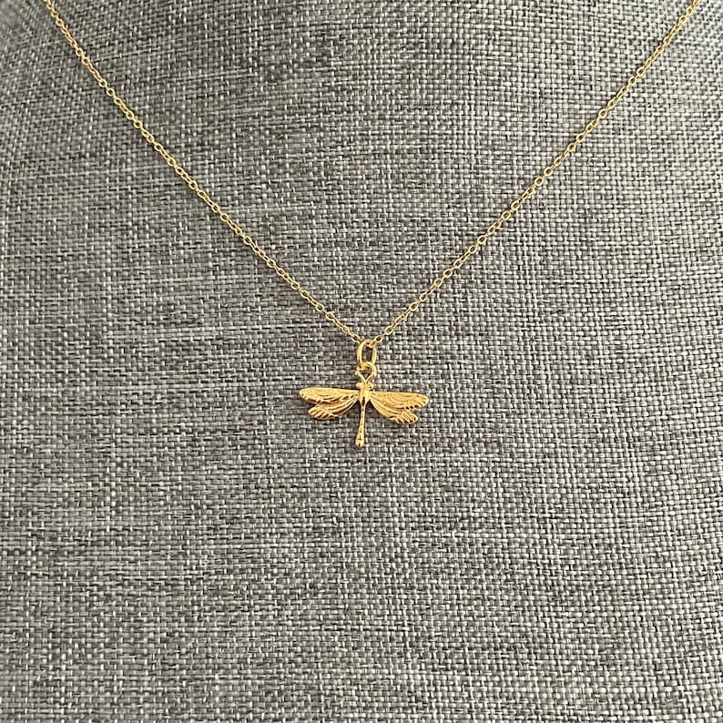 May include: A gold chain necklace with a dragonfly pendant. The dragonfly is detailed and has a delicate design.