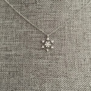 Puede incluir: Un collar de cadena de plata con un colgante de copo de nieve adornado con cristales transparentes.