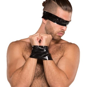 A nude man with dark hair is shown against a blank background. His arms are pulled together in front of him, and his wrists are wrapped together with black Kinklab Bondage Tape. He also has a piece of tape wrapped around his head, covering his eyes.