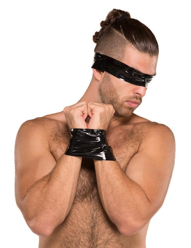 A nude man with dark hair is shown against a blank background. His arms are pulled together in front of him, and his wrists are wrapped together with black Kinklab Bondage Tape. He also has a piece of tape wrapped around his head, covering his eyes.