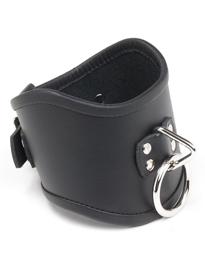 The Tall Curved Posture Collar With A Locking Buckle is shown against a blank background. It is black leather with silver hardware and has a D-ring in the front with an O-ring hanging off of it. The collar has a slight dip at the top in the front.