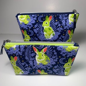 May include: Two zippered pouches with a navy blue background and a repeating pattern of green rabbits, white crescent moons, and gold stars. The pouches have a lime green zipper.