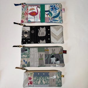 May include: Four zippered pouches with different patchwork designs. The pouches are made of fabric with various patterns, including floral, geometric, and animal prints. The pouches are all approximately the same size and shape.