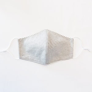 May include: A white face mask with thin black stripes. The mask has white elastic straps.