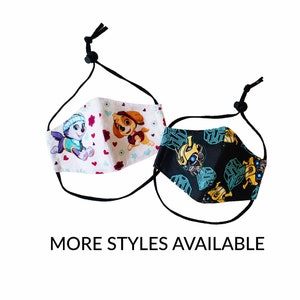 May include: Two adjustable face masks. One mask features cartoon puppies on a white background with red hearts and flowers. The other mask has a black background with a yellow and blue robot design. The text "MORE STYLES AVAILABLE" is below the masks.