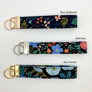 May include: Three keychains with different floral patterns on a white background. The keychains are labeled "Navy Wildwood", "Wild Rose", and "Blue Garden".