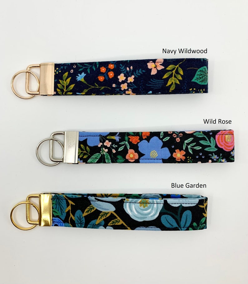 May include: Three keychains with different floral patterns on a white background. The keychains are labeled "Navy Wildwood", "Wild Rose", and "Blue Garden".