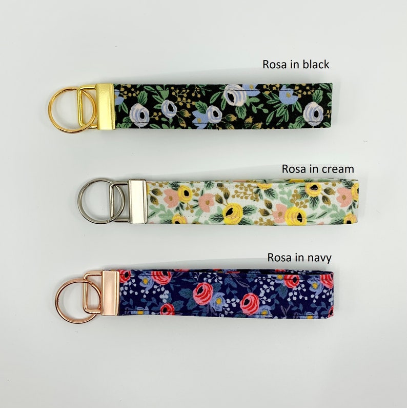 May include: Three keychains with floral patterns. The top keychain has a black background with blue and gold flowers. The middle keychain has a cream background with yellow and pink flowers. The bottom keychain has a navy blue background with pink and red flowers.