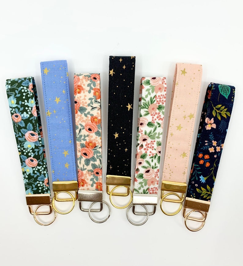May include: Set of eight keychains with different fabric patterns. The keychains feature a gold metal ring and a gold metal clasp. The fabric patterns include floral, stars, and geometric designs. The keychains are a great way to add a touch of personality to your keys.