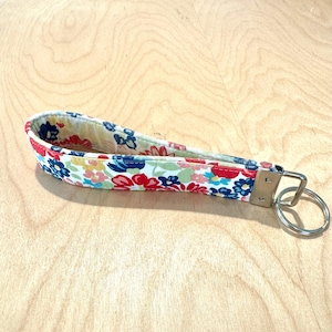 May include: A white fabric key chain with a floral pattern in red, blue, and pink. The key chain has a silver metal ring.