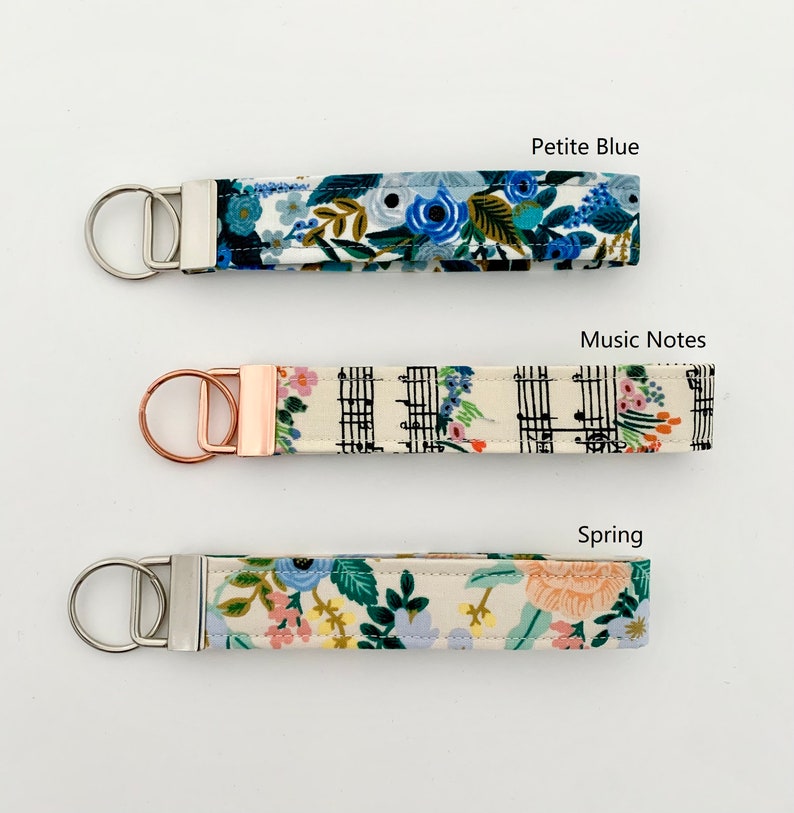 May include: Three keychains with different fabric patterns. The top keychain has a blue floral pattern and the text "Petite Blue". The middle keychain has a black and white music note pattern and the text "Music Notes". The bottom keychain has a floral pattern and the text "Spring".