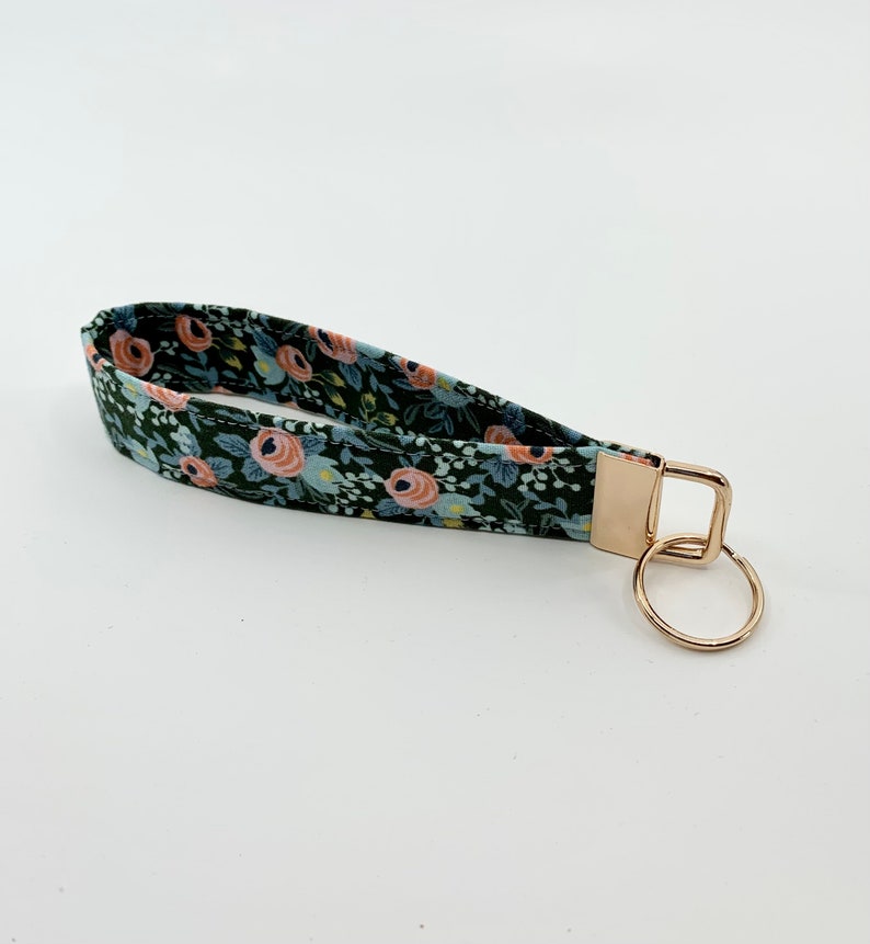 May include: A green fabric key chain with a floral pattern featuring pink and blue flowers. The key chain has a gold metal key ring.