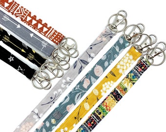 May include: Five colorful fabric keychains with silver key rings. The keychains feature different patterns, including geometric, floral, and abstract designs.
