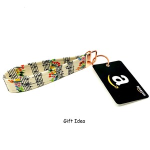 May include: A white and cream key chain with a musical note and floral pattern. The key chain has a rose gold metal ring and clasp. The text "Gift Idea" is printed below the key chain.