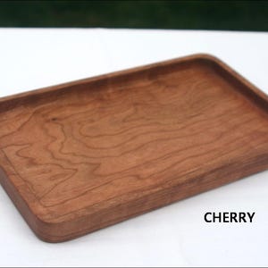 Pode incluir: Uma bandeja retangular de madeira de cerejeira. A bandeja tem uma superfície lisa e polida e bordas arredondadas.