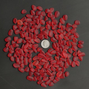May include: A large pile of red glass pebbles, about the size of a UK 20 pence coin, on a black background.