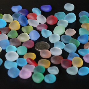 May include: A collection of colourful, frosted glass pebbles in various shades of blue, green, red, pink, and yellow. The pebbles are scattered on a black surface.