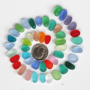 May include: A collection of 30 colorful glass beads in various shades of blue, green, red, orange, yellow, and pink. The beads are arranged in a spiral pattern on a white surface.