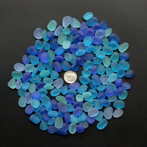 Puede incluir: Una colección de piezas de vidrio de mar azul y turquesa, dispuestas en círculo sobre un fondo negro. El vidrio de mar es liso y pulido, con una variedad de formas y tamaños.