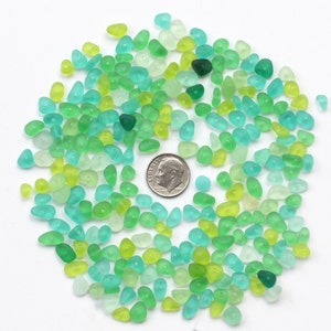 May include: A collection of small, smooth, green, blue, and yellow glass beads. The beads are arranged in a circle around a 10 pence coin.